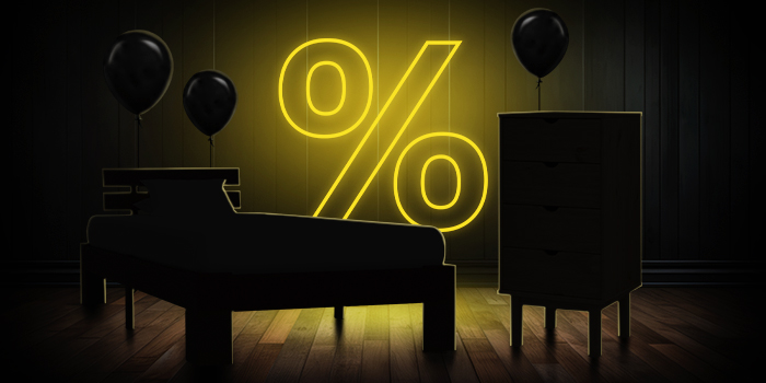 Juoda lova ir komoda su juodais balionais priešais ryškiai geltoną procento ženklą ant tamsaus medinio grindų.